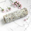 Rolled sage bundle tied with twine on a marble surface with small pink flowers.