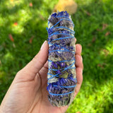 Hand holding a bundle of dried herbs wrapped with blue string against a green grass background