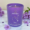 Purple candle with Sagittarius design on a marble surface with purple flowers