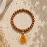 Wooden beaded bracelet with a yellow tassel on a textured beige surface
