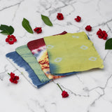 Colorful tie-dye scarves on a marble surface with red flowers and green leaves.