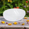 White Selenite bowl on a wooden surface with flower petals and blurred garden background