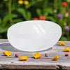 White Selenite bowl on a wooden surface with flower petals and blurred garden background