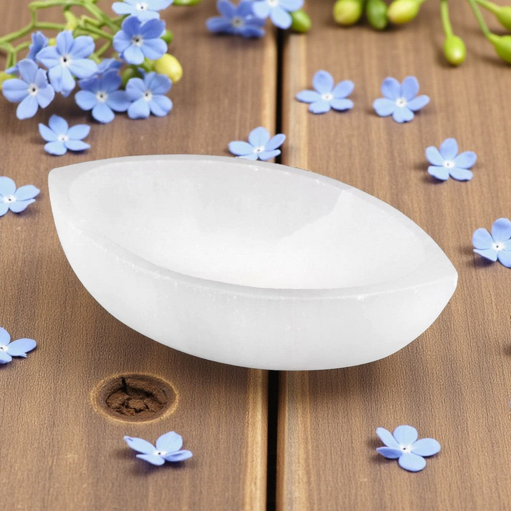 Selenite boat bowl on a wooden surface with small blue flowers around