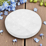 Round selenite charging plate on a wooden surface with blue flowers