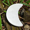 White crescent-shaped selenite charging plate on a natural background with rocks and grass.