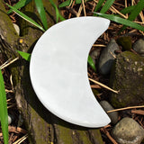 White crescent-shaped selenite charging plate on a natural background with rocks and grass.