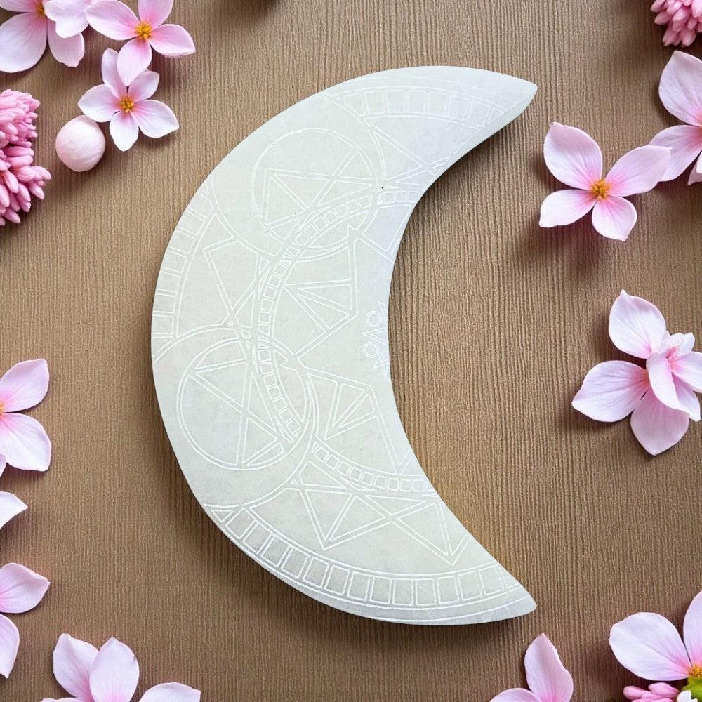 Decorative white crescent moon selenite charging plate on a brown background with pink flowers.