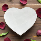 Heart-shaped selenite on a wooden surface with red flower petals