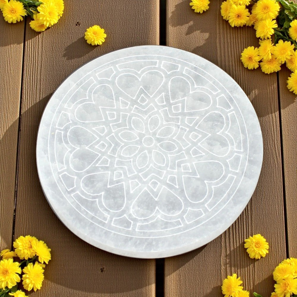 Round selenite charging plate with geometric pattern on a wooden surface with yellow flowers