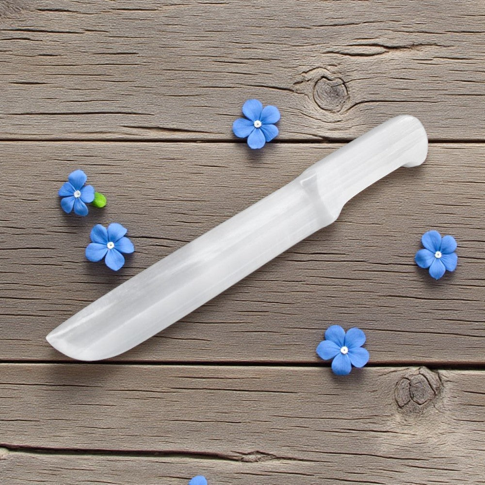 White selenite knife on a wooden surface with blue flowers around it