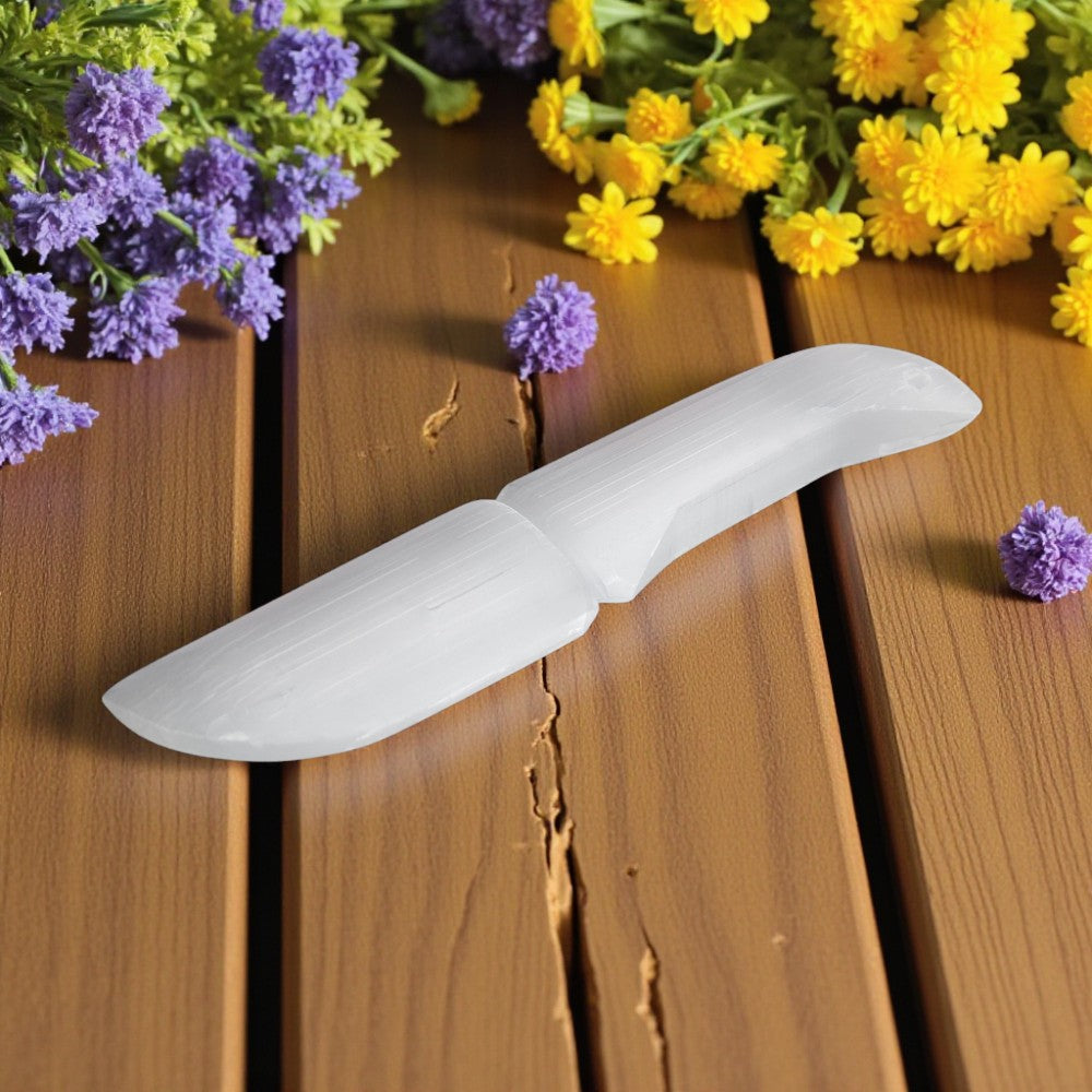 White selenite knife on a wooden surface with purple and yellow flowers.