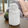 Selenite tower lamp on a wooden table with a blurred living room background