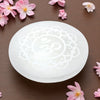 White selenite charging plate with floral design on a brown surface with pink flowers