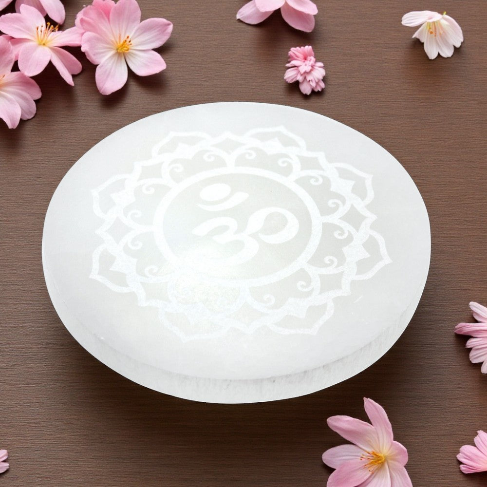 White selenite charging plate with floral design on a brown surface with pink flowers