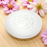 White selenite charging plate with intricate design on a wooden surface with pink flowers.