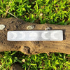Selenite charging plate with moon phase carvings on a wooden branch with green foliage