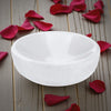 White selenite bowl on a wooden surface with red rose petals