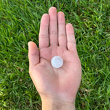 Hand holding a small selenite sphere against a grassy background