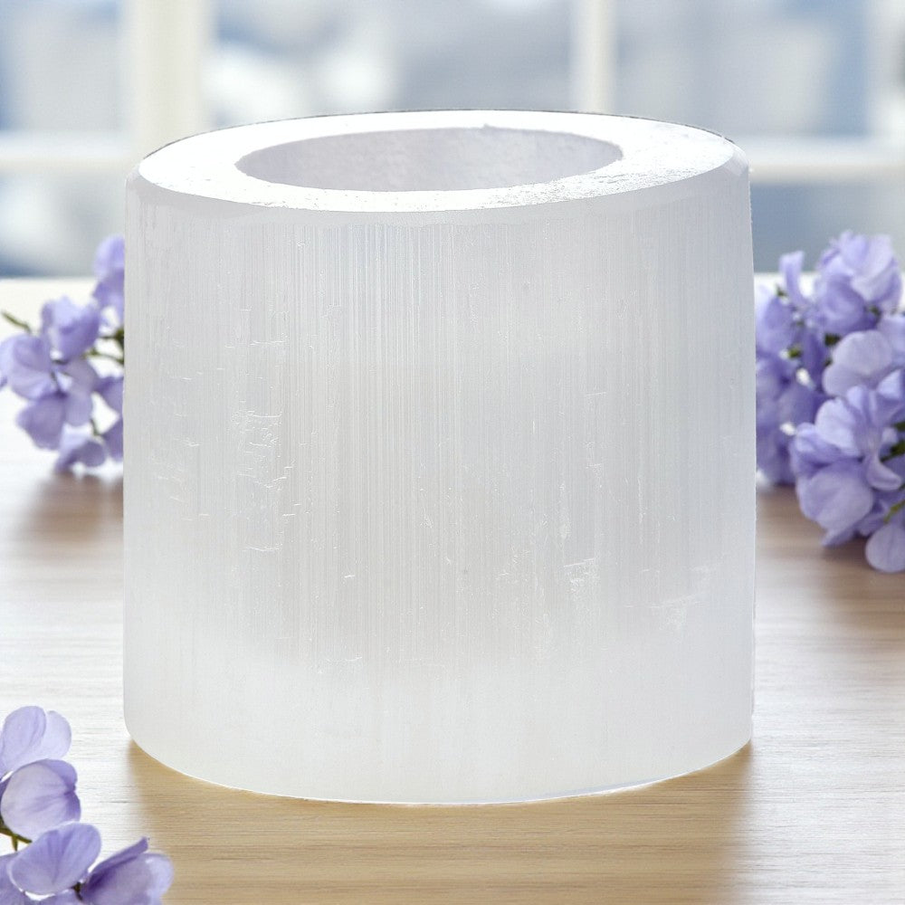 Selenite tea light holder on a wooden surface with purple flowers in the background