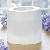 Selenite tea light holder on a wooden surface with purple flowers in the background