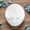 White selenite palm stone with tree of life design on a wooden surface with blue flowers.