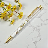 Decorative pen with floral design on a marble surface with yellow flowers.