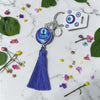 Keychain with blue tassel and decorative tag on a marble surface with flowers and leaves.