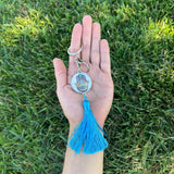 Hand holding a keychain with a blue tassel against a grass background