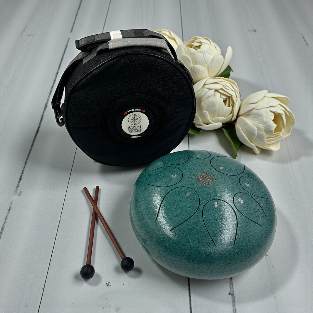 Green Steel Tongue Drum - 10" with carrying case, sticks, and white flowers on a light wooden surface