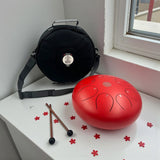 Red Steel Tongue Drum - 10" on a white surface near a window