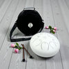White Steel Tongue Drum - 12" carrying bag, mallets, and flowers on a wooden surface