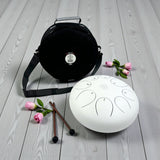 White Steel Tongue Drum - 12" carrying bag, mallets, and flowers on a wooden surface