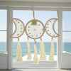 Decorative dreamcatcher with tassels hanging in front of a window with a view of the ocean.
