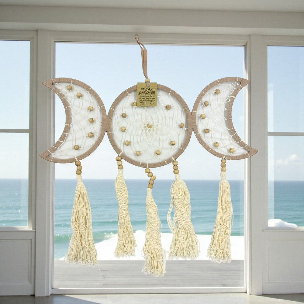 Decorative dreamcatcher with tassels hanging in front of a window with a view of the ocean.
