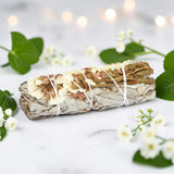 Bundled sage with white twine on a light background with green leaves and flowers.