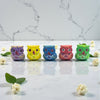 Five colorful owl figurines on a marble surface with flowers.