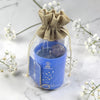 Blue candle in a glass jar with a drawstring bag on a marble surface with white flowers.