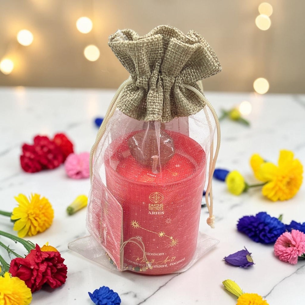 Ariescandle in a clear bag with a decorative bow, surrounded by colorful flowers on a light surface.