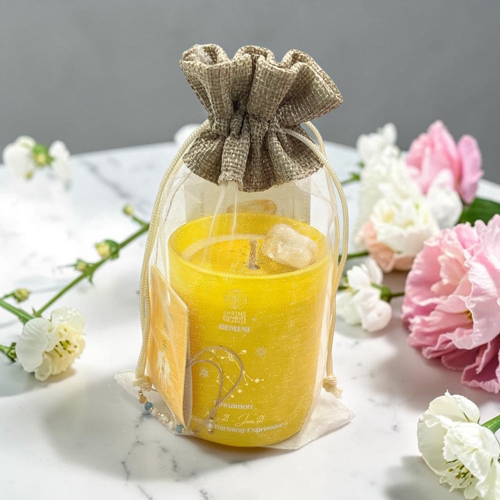 Gemini candle in a drawstring bag with flowers on a marble surface
