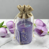 Purple candle in a drawstring bag with purple tulips on a marble surface