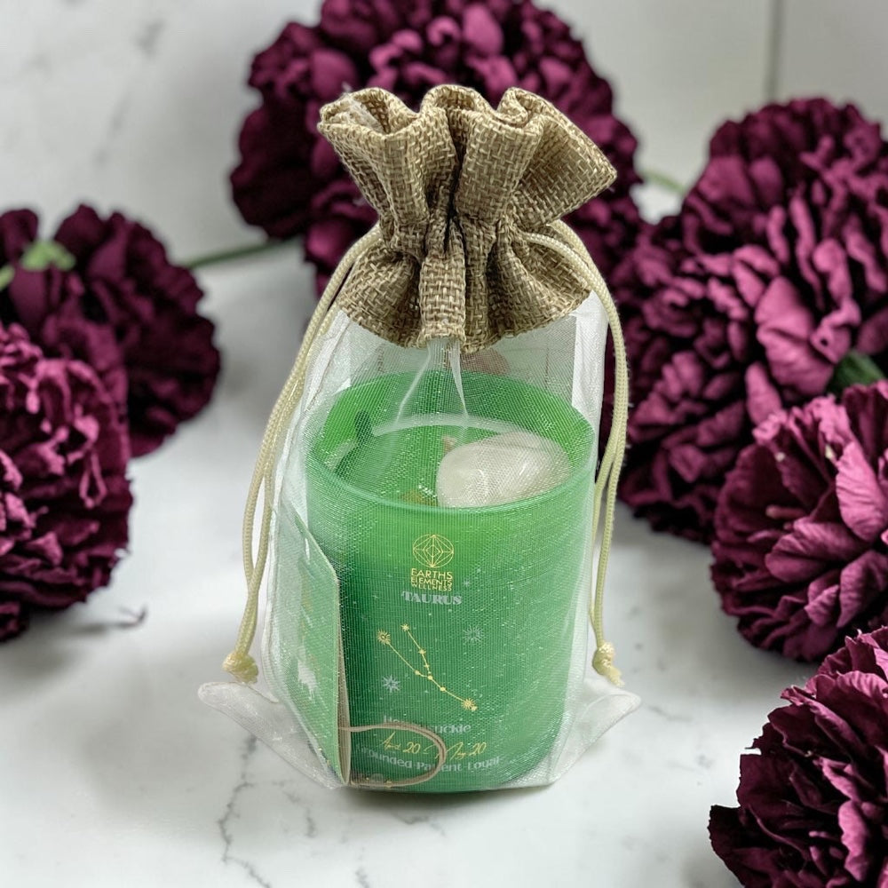 Green candle in a drawstring bag with purple flowers in the background