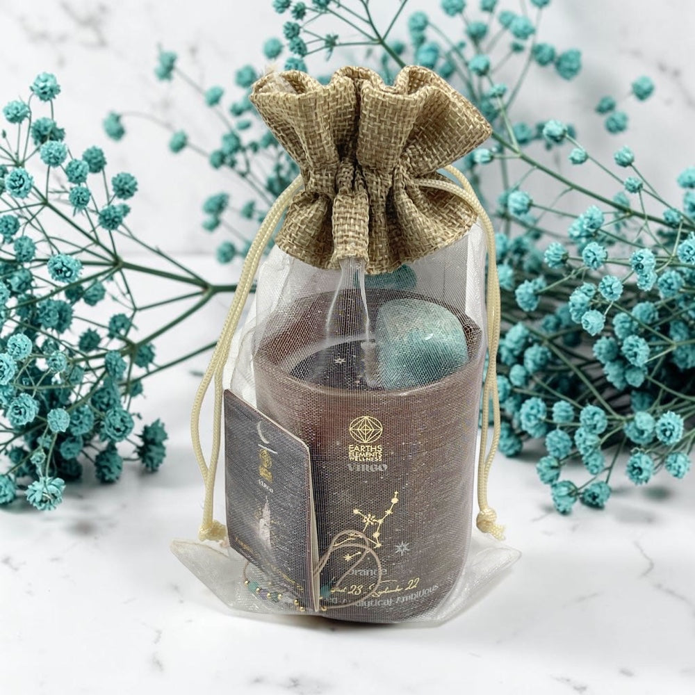 Candle in a decorative brown drawstring bag with flowers in the background