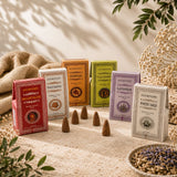 Six boxed herbal blends arranged on a sandy surface with dried flowers, burlap, and leaves around them. The boxes are labeled Ayurvedic Dragon's Blood, Sandal, Nadi Shanti, Lavender, White Sage, and a red box in front reading Ayurvedic Dragon's Blood.