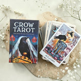Crow Tarot card set with deck and box on a light surface with flowers.