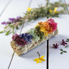Colorful dried flower bundle on a wooden surface with additional flowers in the background.