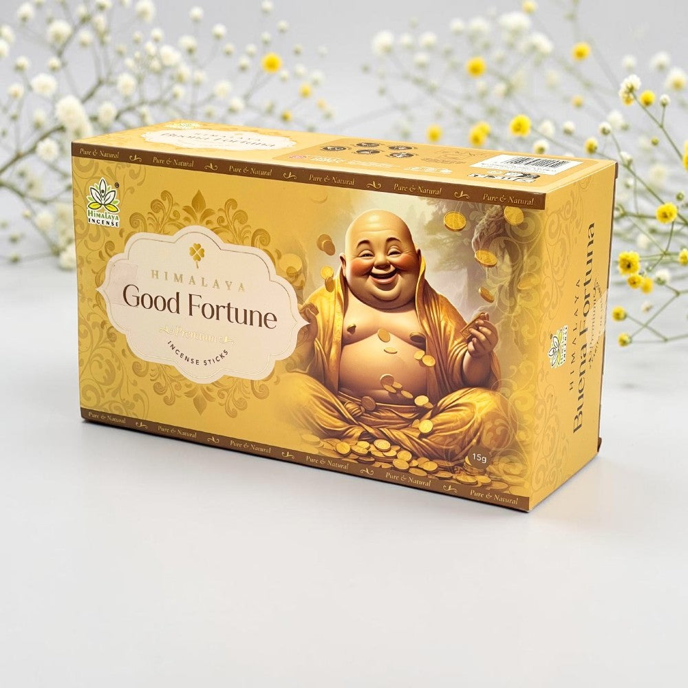A box of Himalaya Good Fortune incense sticks, featuring a golden design with an illustration of a laughing Buddha and gold coins, set against a soft white background with delicate yellow flowers.