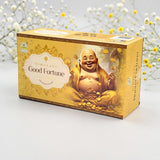 A box of Himalaya Good Fortune incense sticks, featuring a golden design with an illustration of a laughing Buddha and gold coins, set against a soft white background with delicate yellow flowers.
