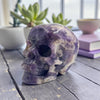 Purple and white stone skull on a wooden surface with plants in the background