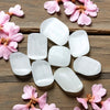 White tumbled selenite on a wooden surface with pink flowers